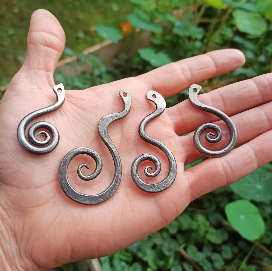 Handgeschmiedete Koru-Spiralanhänger aus Stahl auf der Handfläche zum Größenvergleich – Stahlcraft Marinkovits