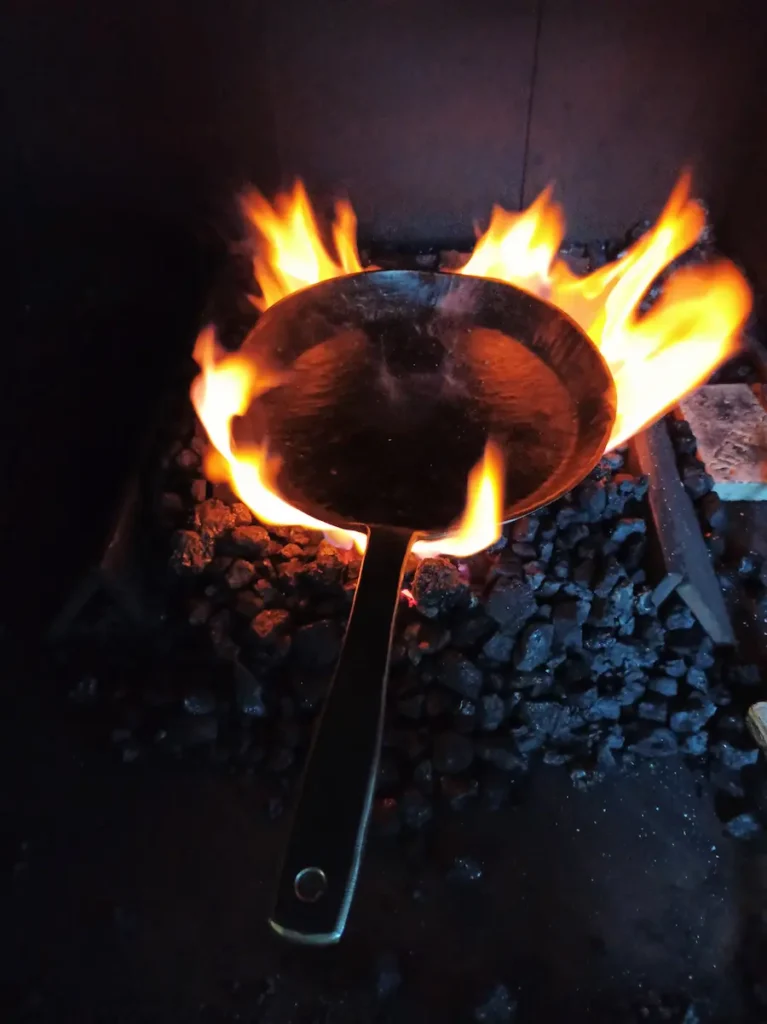 Bratpfanne aus Stahl glüht im Kohlefeuer während der Schmiedearbeit