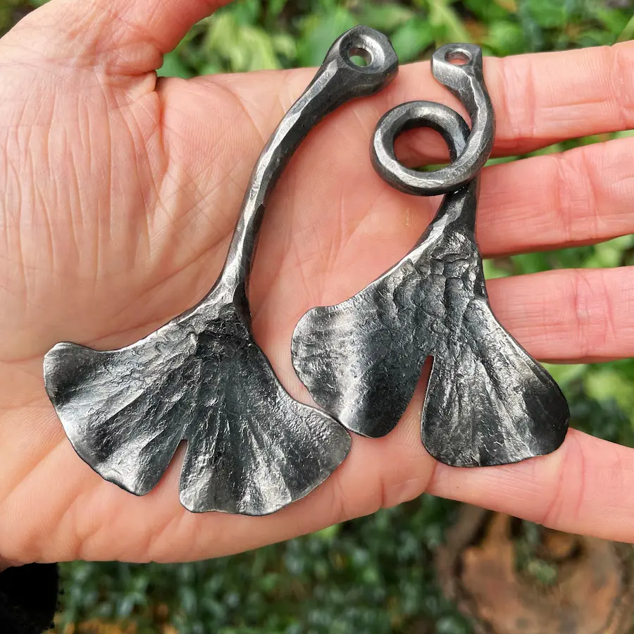 Zwei handgeschmiedete Ginkgoblätter-Anhänger aus Stahl, Größenvergleich in der Hand