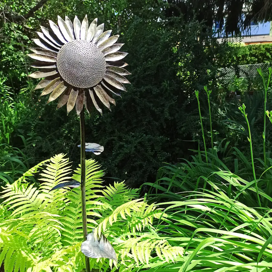 Handgeschmiedete Sonnenblume als Gartendekoration umgeben von Pflanzen